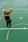 Sênior maduro fêmea em activewear jogando bola em aro enquanto joga basquete em campo de esportes públicos na rua — Fotografia de Stock