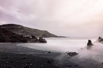 Playa Ciclos contra el mar brumoso y el Volcán Guincho bajo el cielo nublado en Golfo Yaiza Lanzarote Islas Canarias España - foto de stock