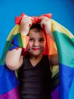 Kleines Mädchen mit gebundener Regenbogenfahne auf dem Kopf blickt vor blauem Hintergrund in die Kamera — Stockfoto