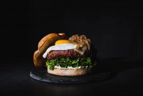 Gustoso hamburger con uovo posto su polpettine e lattuga fresca servito su lavagna su fondo nero in studio — Foto stock
