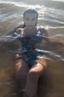 Donna serena con i capelli bagnati nuotare in mare calmo in estate sera e guardando la fotocamera — Foto stock