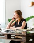 Contenuto artista femminile seduta a tavola con quadri e che parla al cellulare mentre discute di progetto nello spazio di lavoro — Foto stock