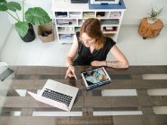 Зверху жіночий графічний дизайнер використовує нетбук і планшет зі стилусом під час роботи над проектом за столом у творчій студії — стокове фото