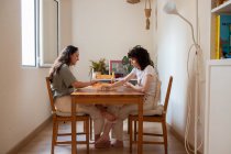 Пара захоплених ЛГБТ-жінок, які сидять за столом і грають в карти, коли розважаються вдома. — стокове фото