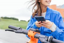 Conteúdo aluguer feminino estacionado scooter elétrico na cidade e navegação telefone móvel — Fotografia de Stock