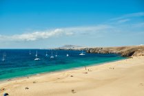 Spiaggia con barche a vela sullo sfondo su un mare turchese sotto un cielo con nuvole nella soleggiata giornata estiva a Fuerteventura, Spagna — Foto stock