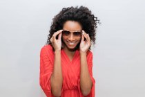Moda jovem afro-americano feminino com cabelos encaracolados em vermelho desgaste e óculos de sol olhando para a câmera — Fotografia de Stock