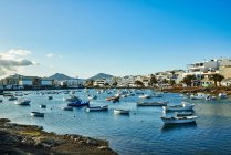 Muitos barcos flutuando em águas fluviais ondulantes perto da cidade contra o céu azul nublado em Fuerteventura, Espanha — Fotografia de Stock