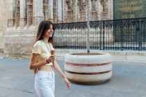 Crop cheerful young female in pendant and earrings with delicious gelato in waffle cone looking away on street — Stock Photo