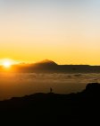 Віддалений вигляд силуету ходунки по скелястому гірському хребту на небо заходу сонця з помаранчевим сонцем — стокове фото