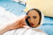 Женское отражение в зеркале в ванной комнате и нанесение крема для лица во время процедуры ухода за кожей утром — стоковое фото