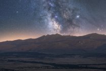Vista panorámica del cielo estrellado con galaxia y gas interestelar sobre magníficas crestas al atardecer - foto de stock