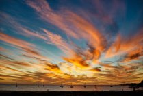 Cielo del atardecer con vívidas nubes anaranjadas situadas sobre el agua de mar con barcos por la noche en Fuerteventura, España - foto de stock
