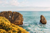 Spektakuläre Szenerie von rauem felsigem Ufer, das von schäumenden Meereswellen im Sonnenlicht unter blauem wolkenverhangenem Himmel in Liencres Kantabrien in Spanien umspült wird — Stockfoto