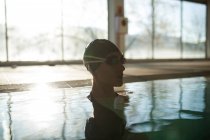 Junge schöne Frau am Bordstein des Hallenbades, mit schwarzem Badeanzug, Sonnenstrahlen, die durch das Fenster eintreten — Stockfoto