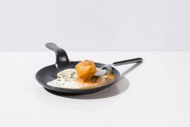 Tenedor de metal con pan fresco sumergido en yema líquida de huevo frito servido en sartén sobre fondo blanco - foto de stock