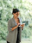 Жінка в окулярах, використовуючи планшет, стоячи в просторому робочому склі з зеленим позаду і працюючи над проектом — стокове фото
