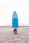 Женщина-серфер сидит с голубой доской SUP на песчаном побережье летом и смотрит в сторону — стоковое фото