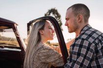 Side view of loving woman touching face of man through opened window of retro car parked in nature in summer evening — Stock Photo