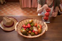 Ama de casa que pesa tomates frescos en jarra de vidrio en balanza de cocina mientras cocina alimentos en casa - foto de stock