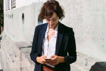 Positivo adulto donna lavoratore esecutivo indossa abito di classe in piedi la navigazione sul cellulare in giornata di sole — Foto stock