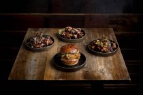 Сверху вкусный бургер с жареными булочками помещен рядом с тарелками с куриными крылышками в соусе барбекю в ресторане — стоковое фото