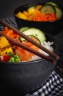Высокий угол азиатского тычка с лососем и рисом с разнообразными овощами подается в миске на столе с палочками в ресторане — стоковое фото