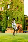 Side view of man lifting black woman while standing on meadow in garden against building with ivy on wall — Stock Photo