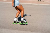Recortado irreconocible ajuste femenino en patines que muestran truco en la carretera en la ciudad en verano - foto de stock
