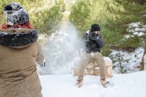 Веселі друзі в теплому одязі грають у сніжки в лісі, насолоджуючись зимовим днем і розважаючись — стокове фото