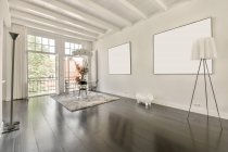 Moderne Loft Home Interior Design mit Esstisch und Stühlen in der Nähe von Fenster in der Ecke des geräumigen Raumes mit Attrappen hängen an der weißen Wand im Haus platziert — Stockfoto
