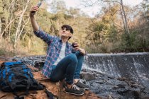 Contenu mâle randonneur avec sac à dos prendre selfie tout en voyageant — Photo de stock