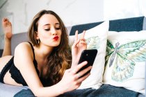 Delighted female in black underwear lying on sofa and messaging on social media via mobile phone in cozy lounge at home — Stock Photo