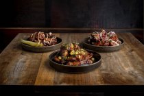 Set di deliziose ali di pollo alla griglia in salsa barbecue servite con verdure su piatti rotondi e poste sul tavolo di legno nel ristorante — Foto stock