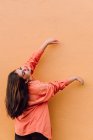 Mujer joven en traje moderno con manicura larga brillante levantando las manos contra fondo naranja - foto de stock