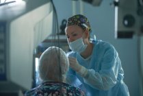 Уважний жіночий хірург у стерильній формі оглядає око анонімного пацієнта проти рефрактометра в лікарні — стокове фото