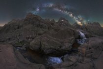 Захватывающий вид высоких грубых гор с каскадом и рекой под звездным небом с галактикой в вечернее время — стоковое фото