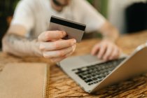 Crop unrecognizable male making purchase with plastic card for order during online shopping via laptop — Stock Photo
