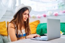 Mujer joven sentada en la mesa y navegando por Internet en netbook disfrutando de fin de semana de verano en la tienda del patio trasero - foto de stock