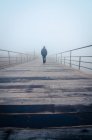 Persona irreconocible paseando por un muelle de madera en una espesa niebla por la mañana en Lisboa, Portugal - foto de stock
