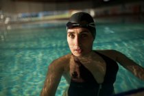 Молодая красивая женщина в закрытом бассейне, в черном купальнике, смотрит в камеру — стоковое фото
