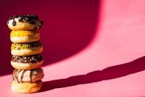 Turm von Donuts in verschiedenen Farben und Geschmacksrichtungen auf rosa Hintergrund — Stockfoto