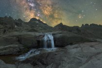 Vista espetacular de altas montagens ásperas com cascata e rio sob céu estrelado com galáxia à noite — Fotografia de Stock