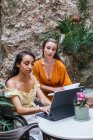 Freelancers femininos multirraciais sentados à mesa no café tropical e trabalhando no projeto enquanto digita na doca de teclado do tablet — Fotografia de Stock