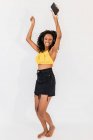 Счастливая афроамериканка в наушниках с сотовым телефоном танцует, слушая песню на светлом фоне — стоковое фото