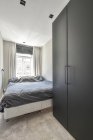 Интерьер современной светлой спальни с мягкой кроватью и деревянным шкафом расположен на ковре возле окна с занавесками и телевизором в углу — стоковое фото