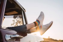 Side view of crop female chilling in vintage car with legs sticking out of window in evening in nature — Stock Photo