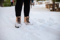 Cosechar hembra irreconocible en botas calientes de pie en el suelo cubierto de nieve en el día de invierno - foto de stock