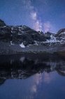 Vista pitoresca do céu estrelado com galáxia refletindo em lago contra monte com neve ao entardecer — Fotografia de Stock