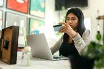 Mujer haciendo la compra con tarjeta de plástico para la orden durante las compras en línea a través de ordenador portátil - foto de stock